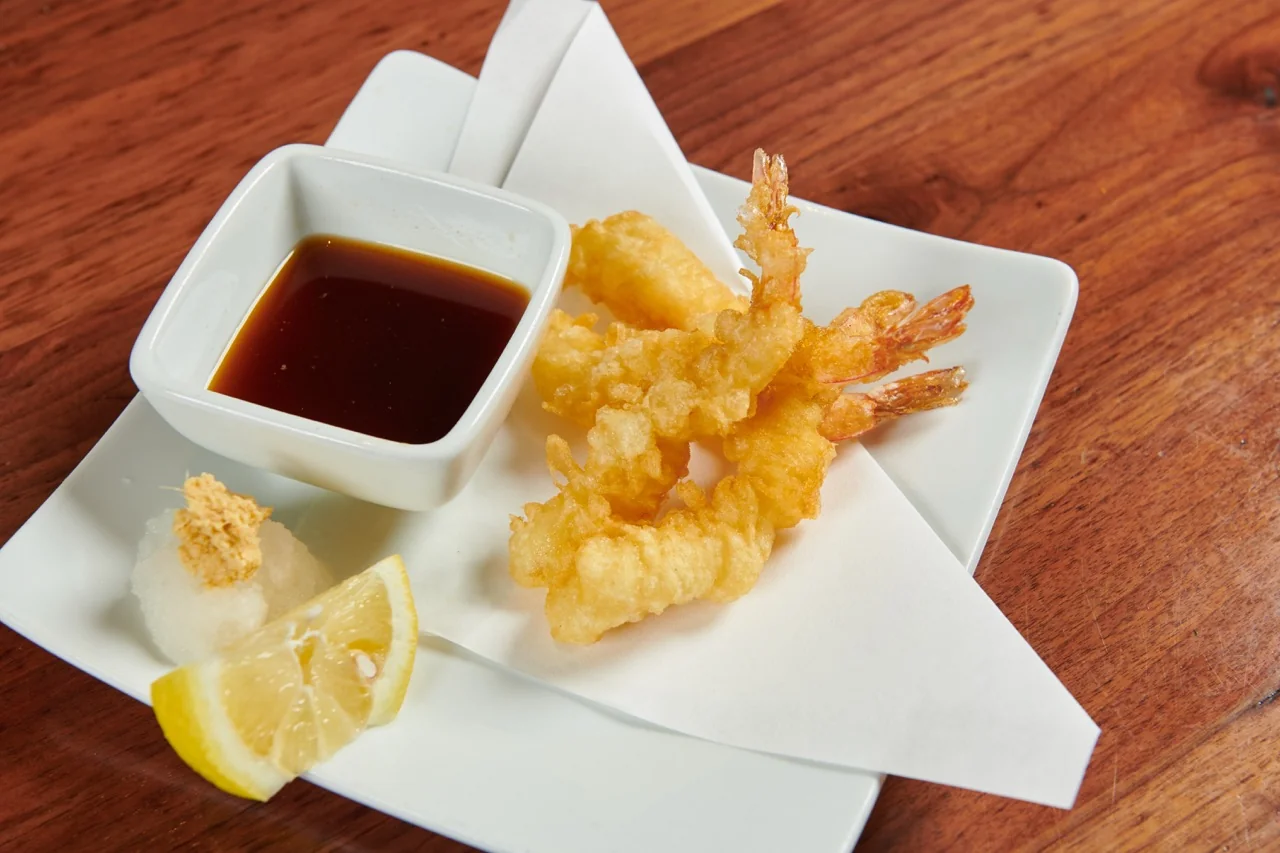 Shrimp tempura on a white plate, with a dish of dipping sauce, grated daikon and a lemon wedge.