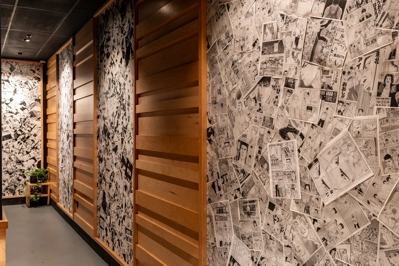A corridor at College Heights papered floor to ceiling with black and white manga pages, broken up by panels of maple slats.