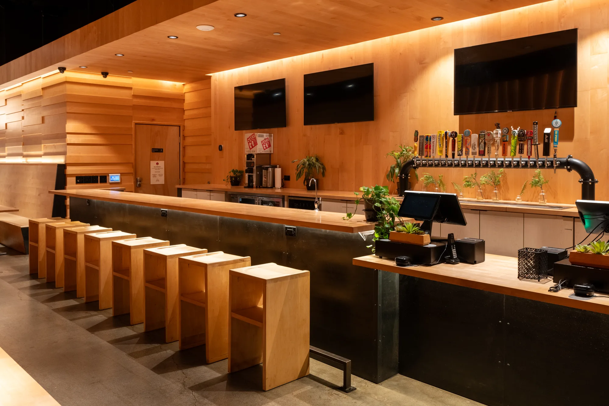 The ramen bar at College Heights. A row of maple stools runs along a maple counter, with the craft beer tap wall and its row of tap handles behind it.