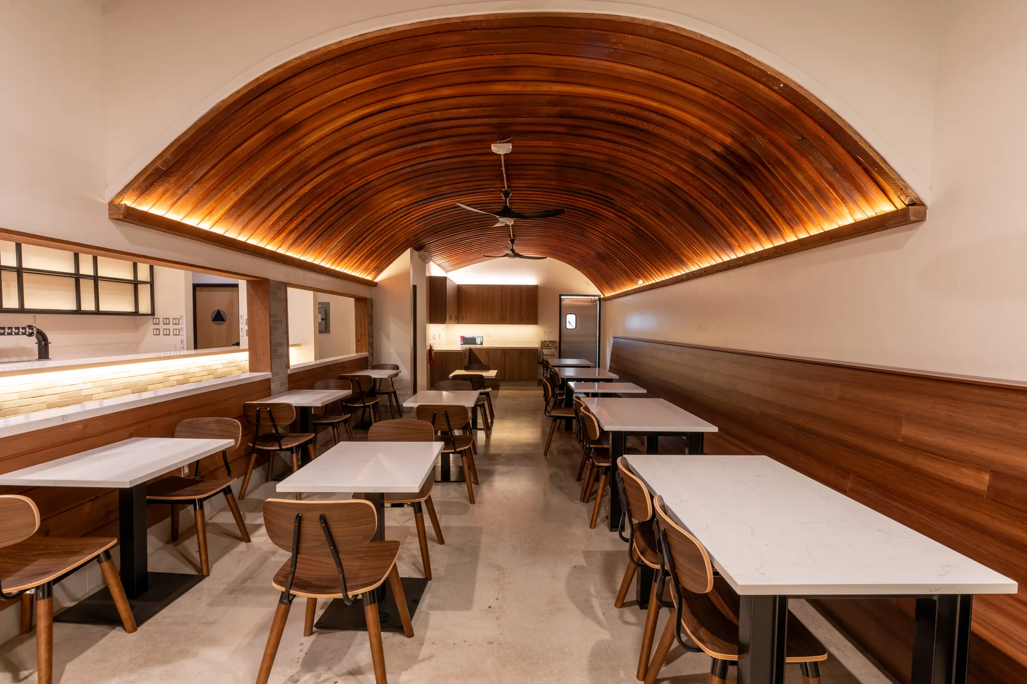 The Crown Point dining room before service. Tables and wooden chairs sit under a barrel-vaulted ceiling of curved wood slats lit from behind, with the service counter running along the left wall.