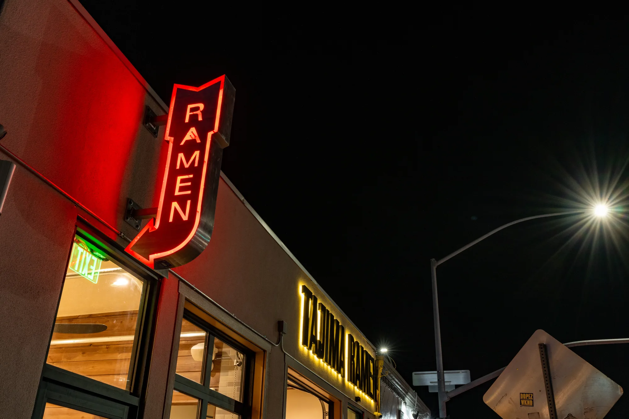 The red neon RAMEN arrow mounted on the corner of the Tajima Crown Point building at night, with the lit Tajima Ramen sign running along the storefront behind it.