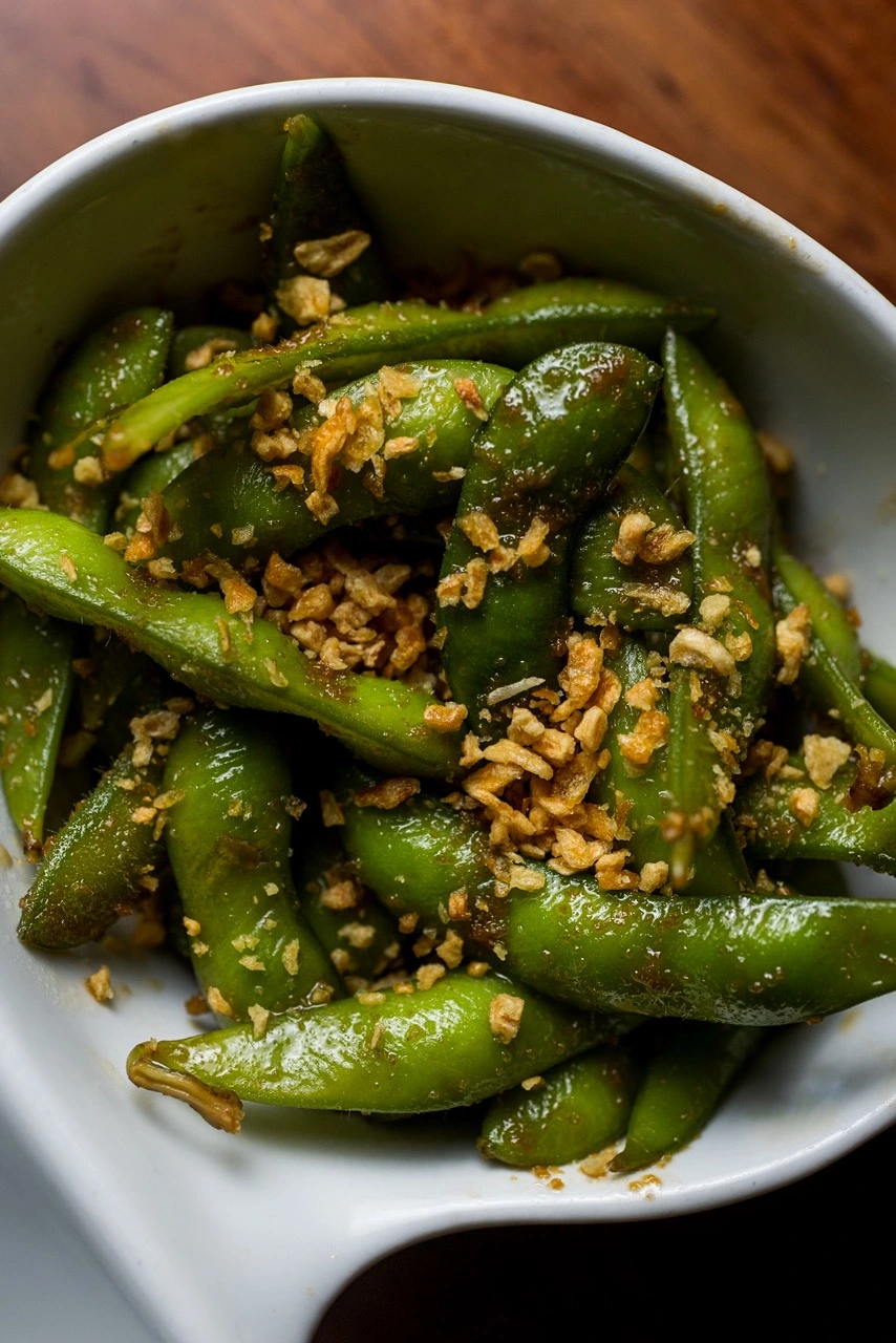 Garlic Edamame, edamame pods in a white bowl, glossed with sauce and scattered with fried garlic