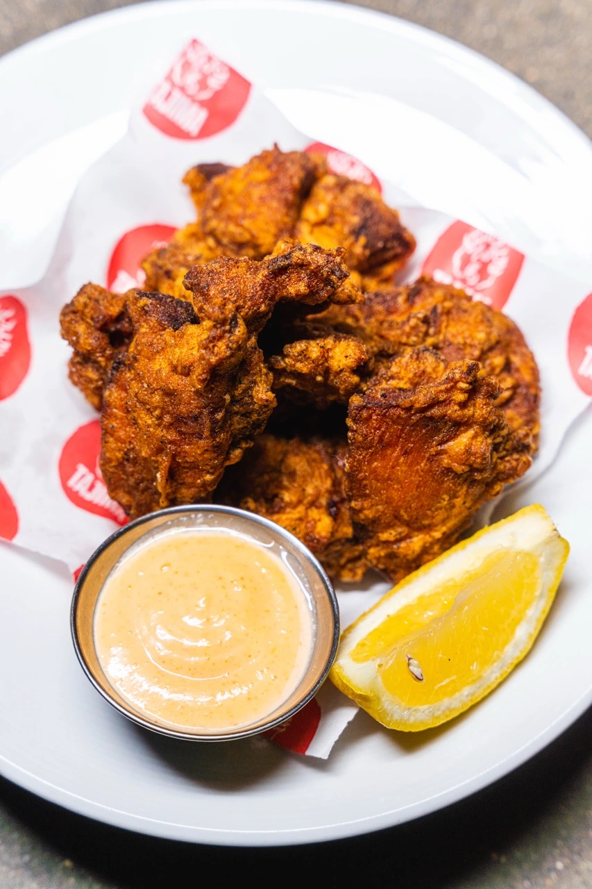 Karaage, pieces of seasoned fried chicken on Tajima-branded paper, with a cup of mayonnaise and a lemon wedge