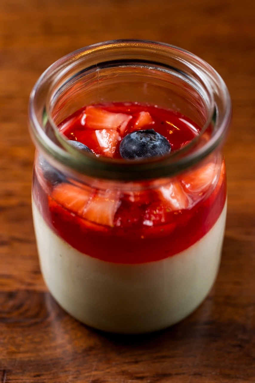 Matcha Panna Cotta in a glass jar, a pale green set cream under red berry compote with strawberry pieces and blueberries